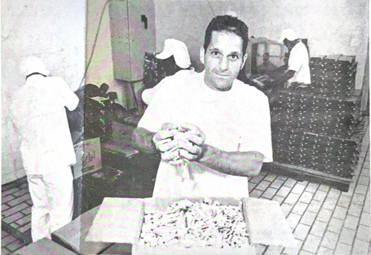 Venicius Tobias, de touca e avental branco, mexendo produto numa mesa da fábrica
